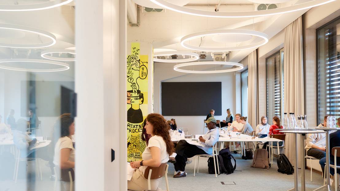 mehrere Teilnehmende sitzen an einem langen Tisch und arbeiten